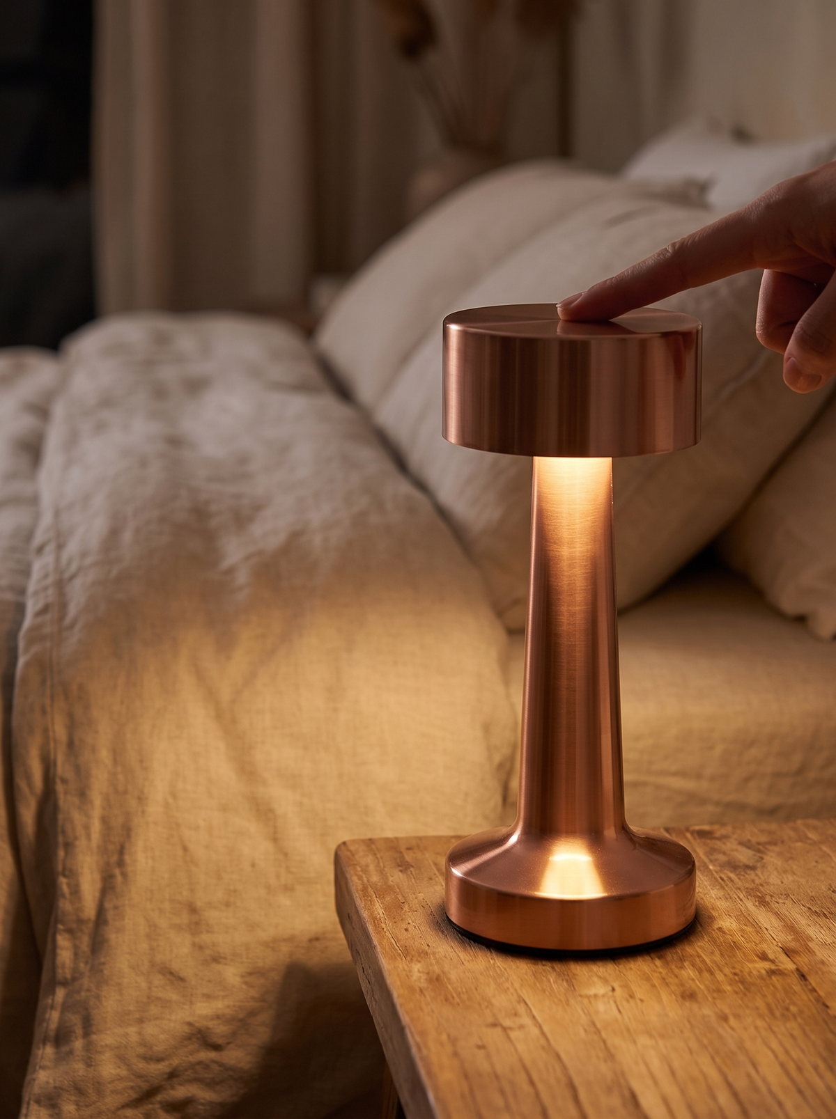 Finger touching the top of the cordless table lamp to dim it beside a bed