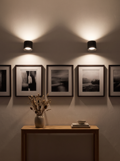 Two cordless wall lights washing light over a hallway gallery wall